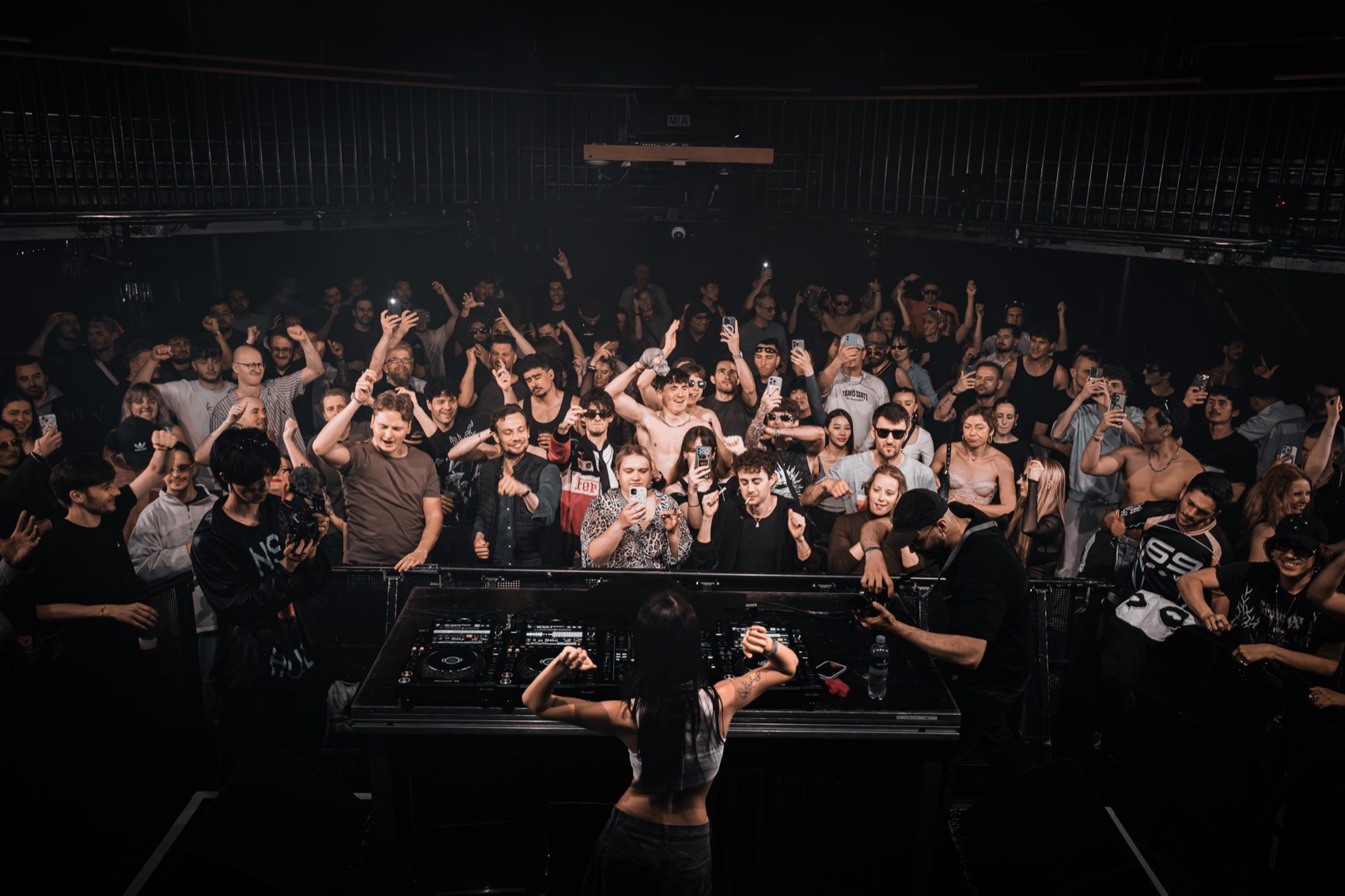 The whole room with hands up, seen from behind the booth